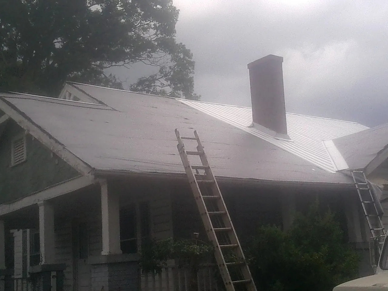 Ladders against a metal roof on an older home with a brick chimney in Mead