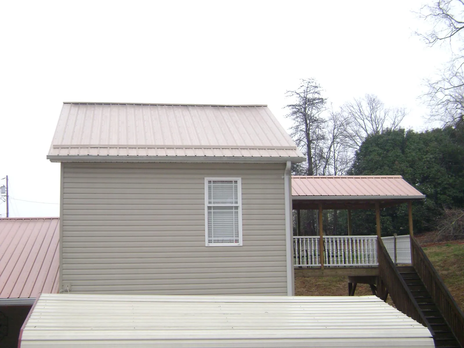 Tan metal roofs on a two story addition and attached porch, from a Roof Replacement job in Mead